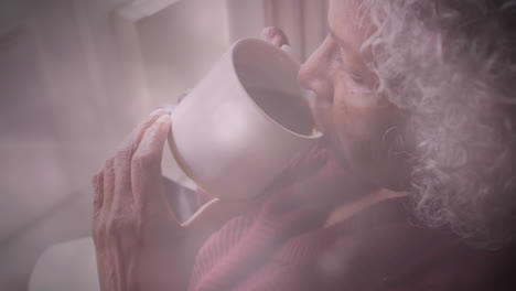 Animation-of-glowing-light-over-pensive-senior-woman-drinking-tea