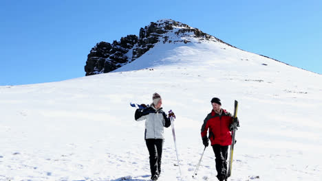 Sporty-couple-walking-down-the-ski-slope