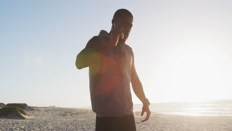 African-american-man-checking-smartwatch,-exercising-outdoors-by-seaside