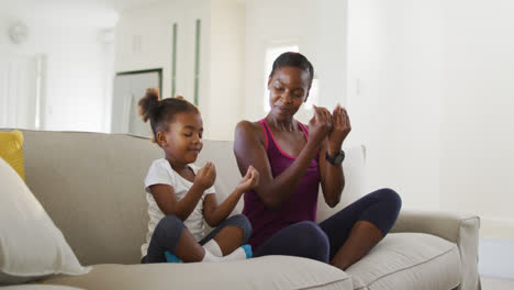 Happy-african-american-mother-and-daughter-sitting-on-sofa-doing-yoga-exercise-at-home
