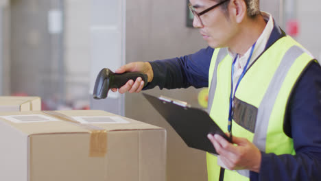 Asian-male-worker-wearing-safety-suit-and-scanning-boxes-in-warehouse