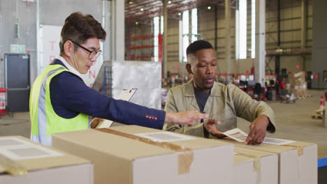 Diverse-male-workers-with-clipboard-and-boxes-talking-in-warehouse
