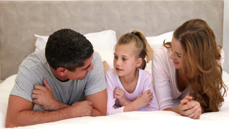 Parents-and-daughter-lying-on-bed-chatting