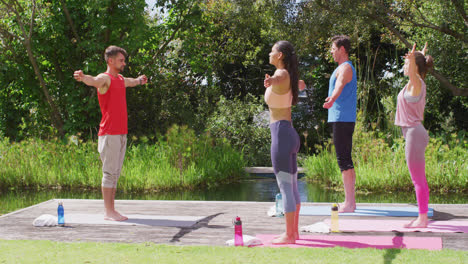 Rear-view-of-caucasian-male-instructor-practicing-yoga-pose-with-diverse-group-in-park