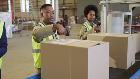 Diverse-male-and-female-workers-wearing-safety-suits-and-scanning-boxes-in-warehouse