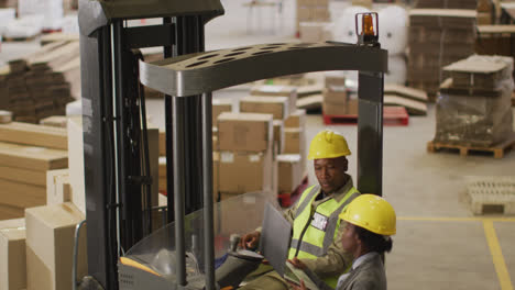 African-american-male-and-female-workers-wearing-safety-suits-and-using-laptop-in-warehouse
