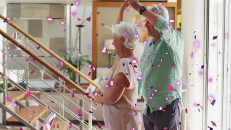 Animation-of-pink-and-purple-confetti-falling-over-happy-caucasian-senior-couple-dancing-at-home