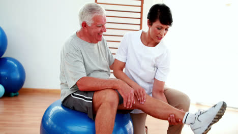 Lächelnder-Physiotherapeut-Hilft-älteren-Patienten-Beim-Beugen-Der-Knie