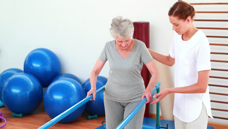 Physical-therapist-helping-patient-walk-with-parallel-bars