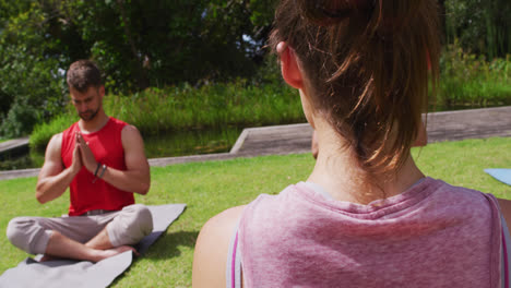 Vista-Trasera-De-Una-Instructora-Caucásica-Practicando-Yoga-Con-Un-Grupo-Diverso-En-El-Parque.
