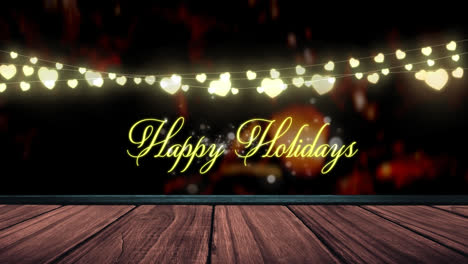 Happy-holidays-text-and-glowing-yellow-heart-shaped-fairy-light-decoration-over-wooden-plank