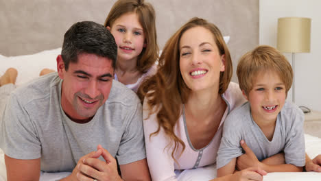 Parents-and-children-lying-on-bed-smiling-at-camera