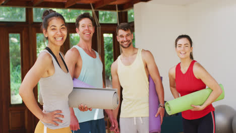 Portrait-of-happy,-diverse-group-of-men-and-women-holding-rolled-up-mats-after-yoga-class-in-studio