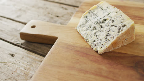 Video-of-wedge-of-blue-cheese-on-chopping-board,-on-rustic-wooden-table