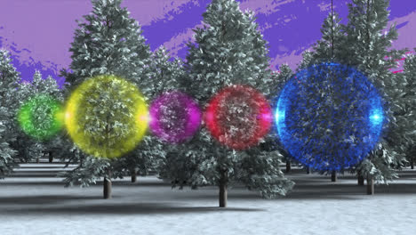 Colorful-bauble-decorations-hanging-over-trees-on-winter-landscape-against-purple-background