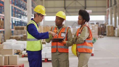 Diverse-male-and-female-workers-wearing-safety-suits-and-talking-in-warehouse