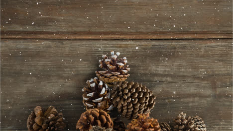 Animation-of-snow-falling-over-pine-cones-on-wooden-table