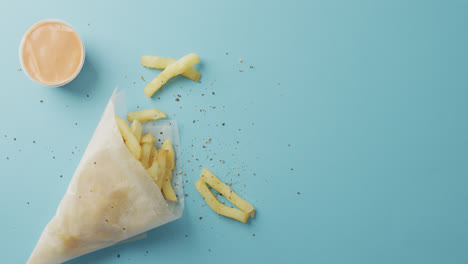 Video-of-chips-wrapped-in-paper,-salt-and-pepper-and-dip,-with-copy-space-on-blue-background
