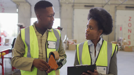 African-american-male-and-female-workers-with-clipboard-talking-in-warehouse