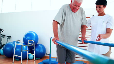 Smiling-physiotherapist-helping-patient-walk-with-parallel-bars