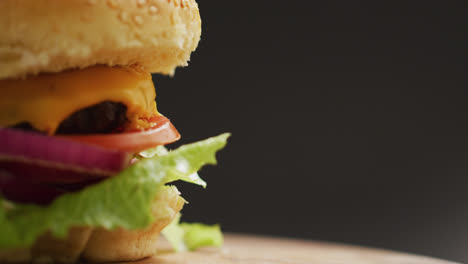 Video-close-up-of-cheeseburger-with-salad-in-burger-bun,-on-grey-background-with-copy-space