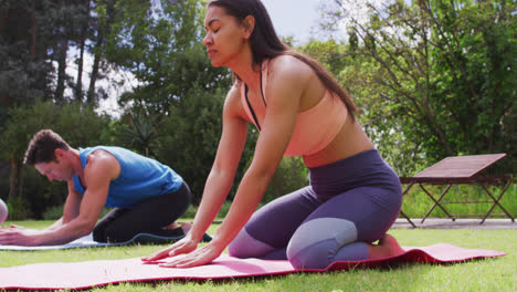 Diverse-group-of-men-and-women-practicing-yoga-pose-kneeling-on-mats-in-park