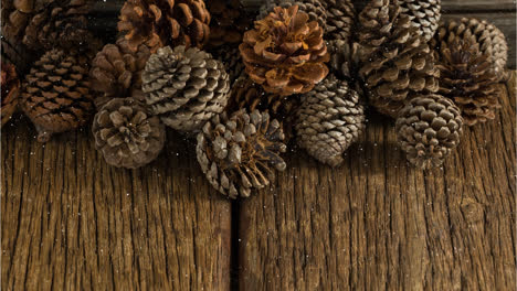 Snow-falling-over-multiple-pine-cones-on-wooden-surface