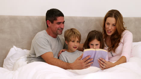 Glückliche-Eltern-Und-Kinder-Lesen-Zusammen-Im-Bett