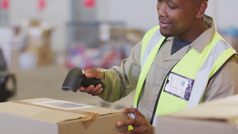 African-american-male-worker-wearing-safety-suit-and-scanning-boxes-in-warehouse