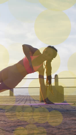 Animation-of-yellow-spots-over-biracial-woman-exercising-on-promenade