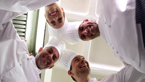 Team-of-chefs-standing-in-circle-looking-down-at-camera