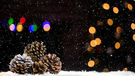 Snow-falling-over-multiple-pine-cones-against-colorful-spots-of-light-on-black-background