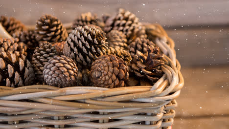 Snow-falling-over-multiple-pine-cones-in-a-basket-on-wooden-surface