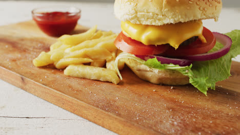Video-of-cheeseburger,-chips-and-bowl-of-ketchup-on-wooden-board