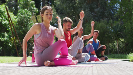Diverse-male-and-female-group-practicing-yoga-sitting-in-a-row-with-eyes-closed-in-sunny-park