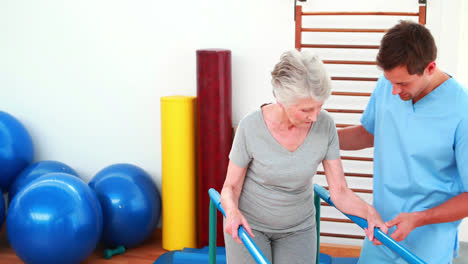 Physical-therapist-helping-patient-to-walk-with-parallel-bars