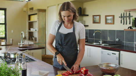 Happy-caucasian-pregnant-woman-wearing-apron-and-cutting-red-pepper