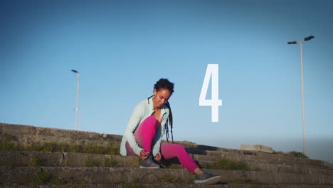 Number-countdown-against-african-american-fit-woman-tying-her-shoe-laces-sitting-on-the-stairs