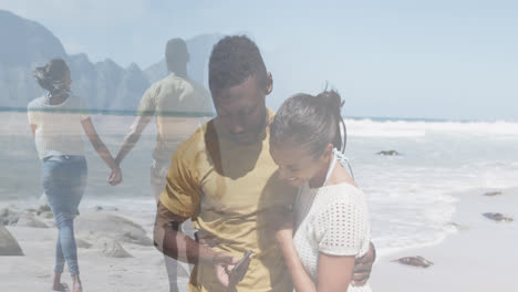 Komposit-Aus-Glücklichem-Afroamerikanischen-Paar,-Das-Smartphone-Benutzt-Und-Händchen-Haltend-Am-Strand-Spaziert