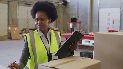 Portrait-of-african-american-female-worker-wearing-safety-suit-and-smiling-in-warehouse