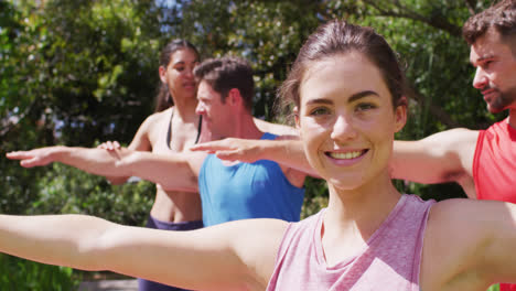 Smiling-caucasian-woman-practicing-yoga-with-diverse-group-and-female-instructor-in-sunny-park