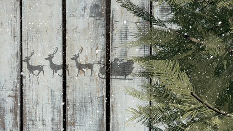 Tree-branches-and-santa-claus-in-sleigh-being-pulled-by-reindeers-against-wooden-plank