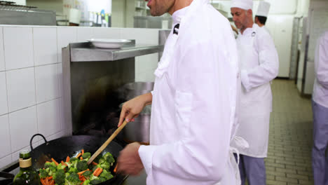Smiling-chef-frying-vegetables-in-a-wok-and-adding-oil