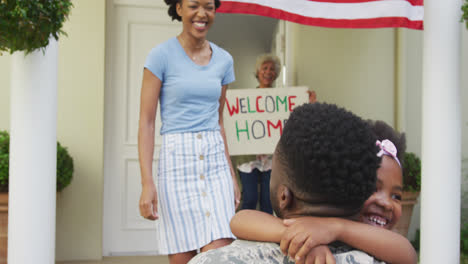 African-american-male-soldier-embracing-his-smiling-wife-and-daughter-with-american-flag