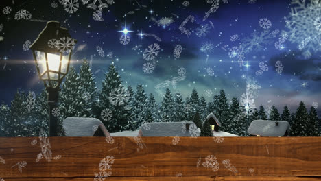 Snowflakes-over-wooden-plank-against-snow-falling-on-winter-landscape-and-night-sky