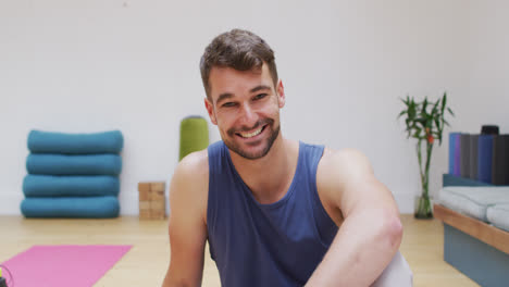 Porträt-Eines-Lächelnden-Kaukasischen-Männlichen-Yogalehrers,-Der-Im-Fitnessstudio-Sitzt