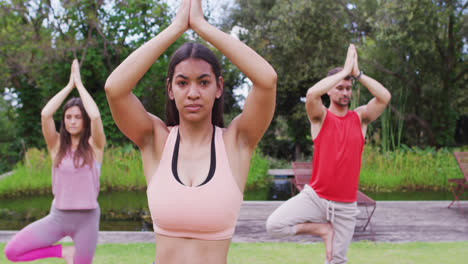 Diverse-group-of-men-and-women-practicing-yoga,-standing-on-one-leg-in-park