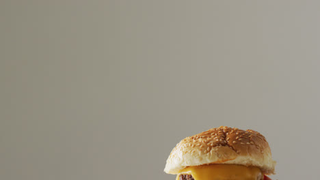 Video-close-up-of-cheeseburger-with-salad-in-burger-bun,-on-pale-grey-background-with-copy-space