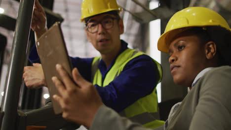 Diverse-male-and-female-workers-wearing-safety-suits-and-using-tablet-in-warehouse