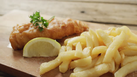 Video-of-fish-and-chips-with-lemon-wedge-on-wooden-board,-on-rustic-table